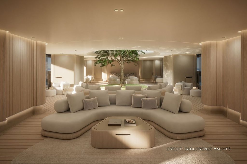 Geschwungene Lounge-Sitzgruppe um einen niedrigen Tisch im Salon einer Superyacht, im Hintergrund ein echter Baum als Blickpunkt