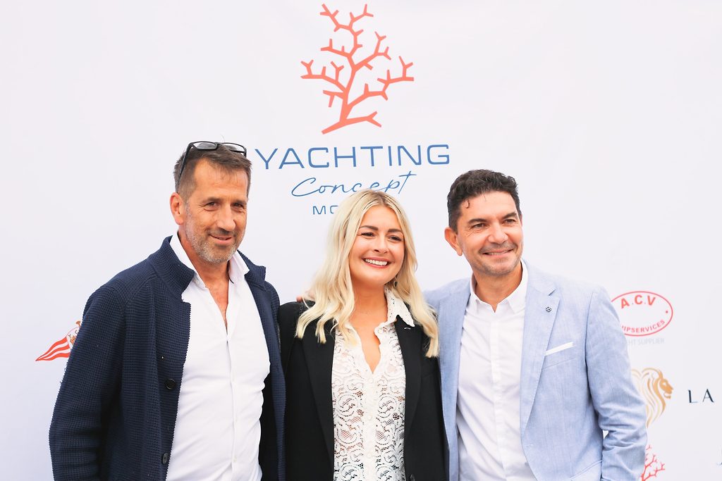 Двое мужчин и женщина позируют на мероприятии на фоне баннера Yachting Concept Monaco