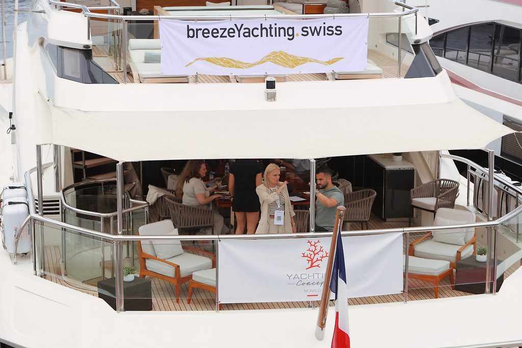 Гости на кормовой палубе моторной яхты с баннером breezeYachting.swiss, в марине