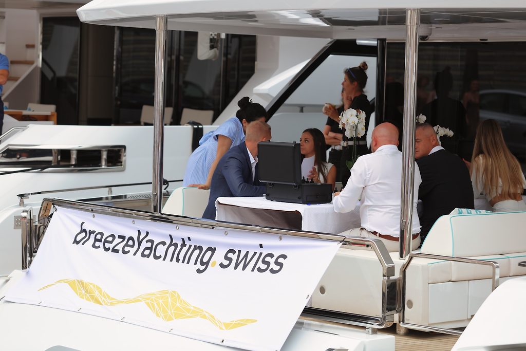 Гости сидят на кормовой палубе моторной яхты, на переднем плане баннер breezeYachting.swiss