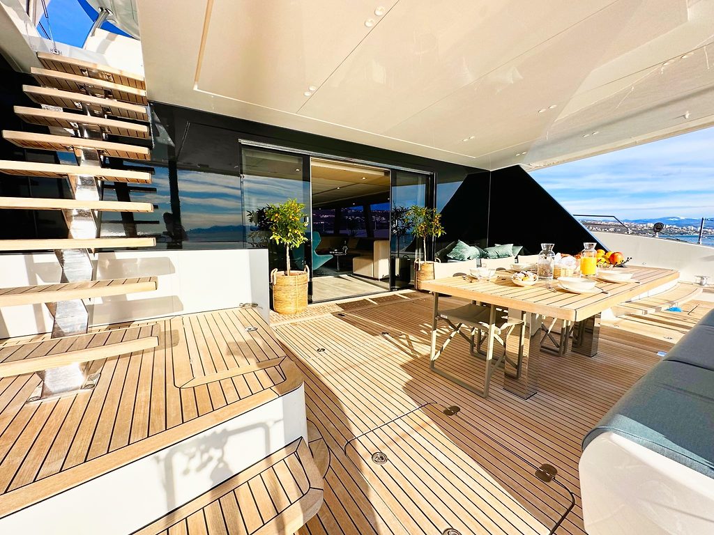 Cubierta de popa de teca con mesa puesta para desayunar en un catamarán, escalera al puente superior