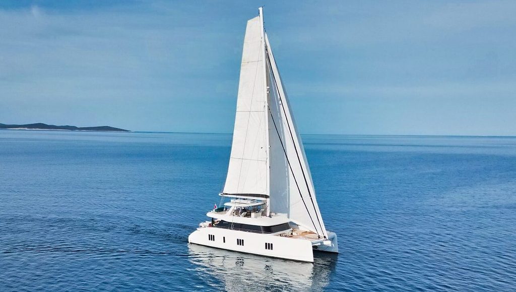 Catamarán de vela con la vela mayor izada, navegando en mar abierto cerca de la costa