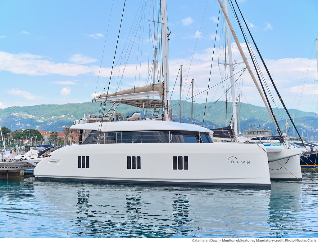 Sunreef 60 sailing catamaran named Dawn, moored in a marina with hills in the background