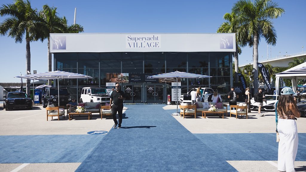 Entrance to the Superyacht Village pavilion with blue carpet and lounge seating, palm trees framing the facade