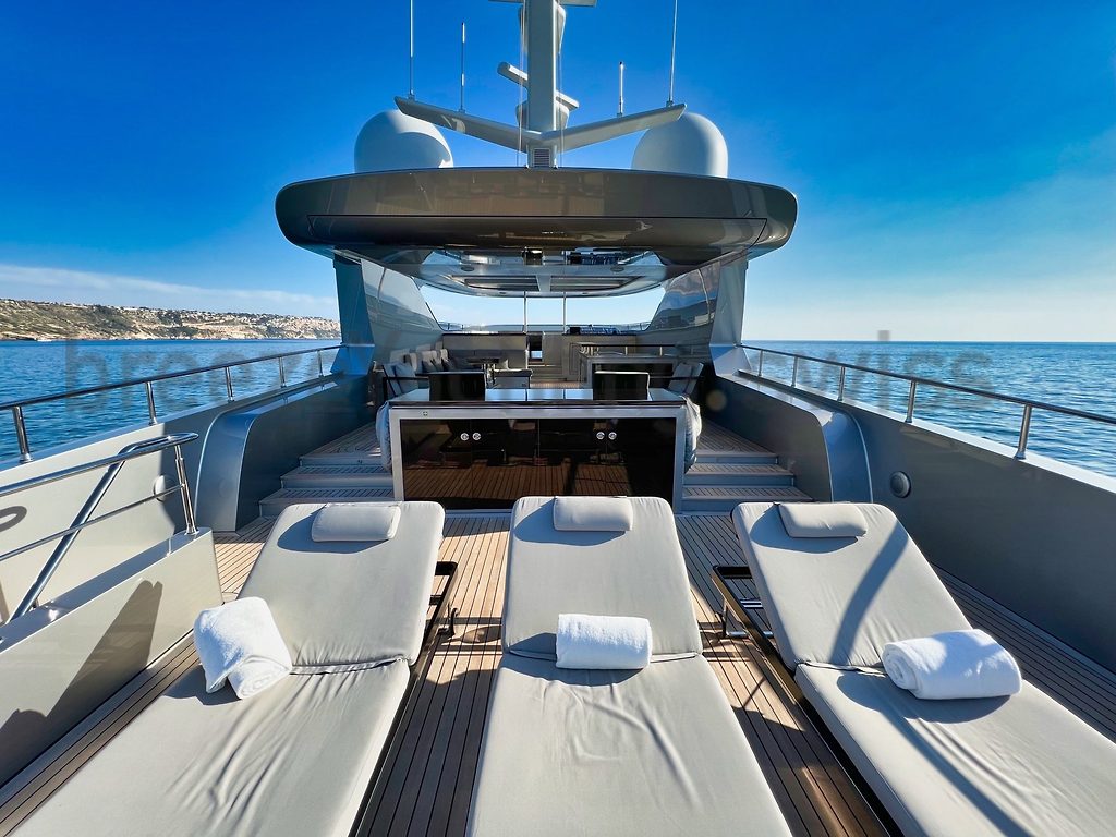 Foredeck sun loungers on a motor yacht, with teak deck and coastline in the background